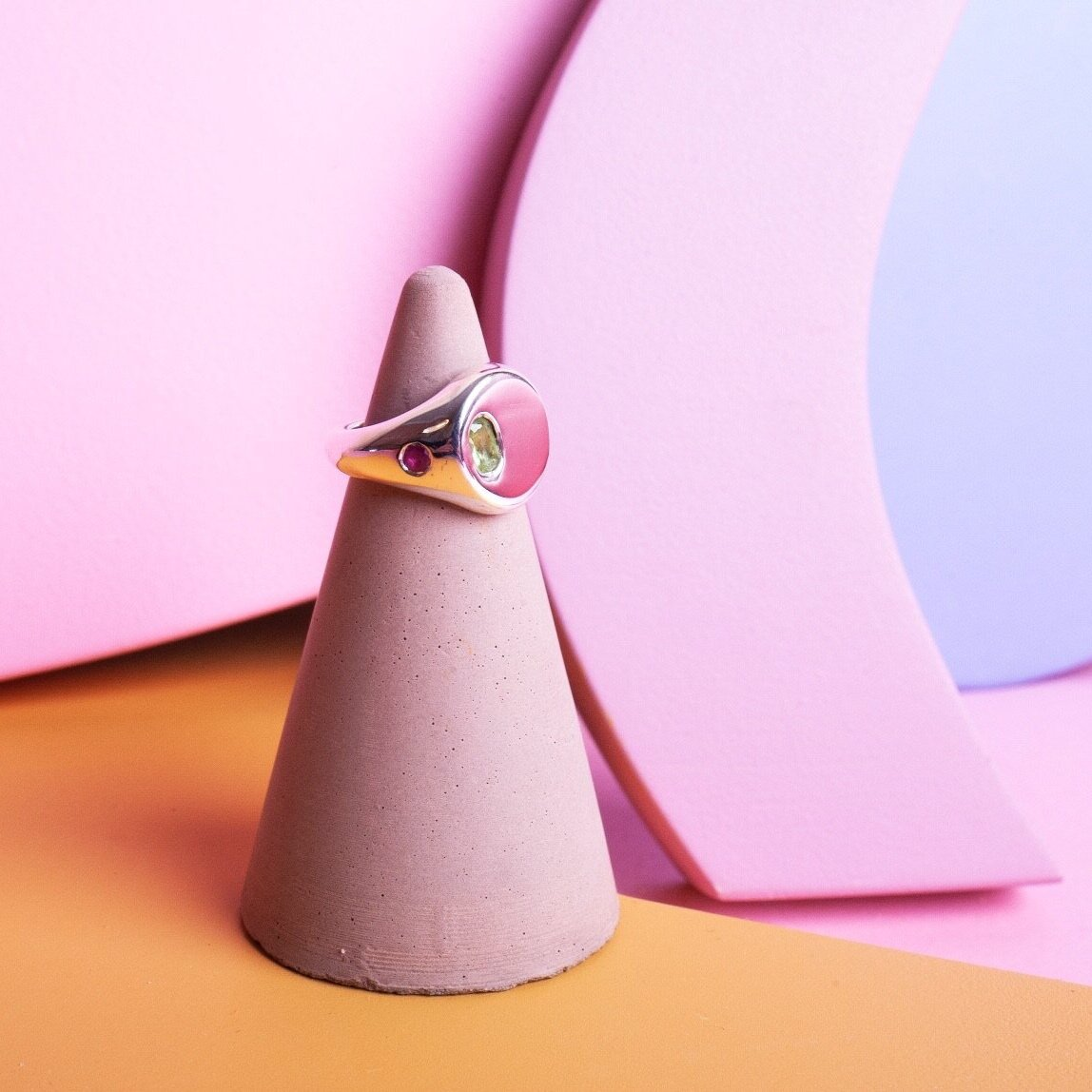 Silver signet ring with a pink gem on the side and a larger green gem in the center