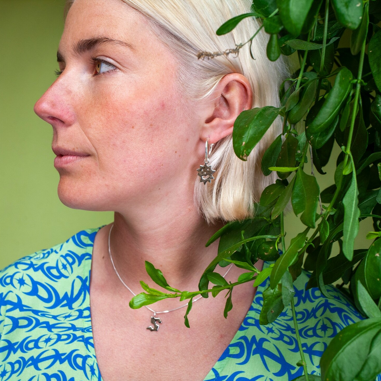 Woman wearing small hoop earring with an irregular spikey shaped charm with a smiling face on