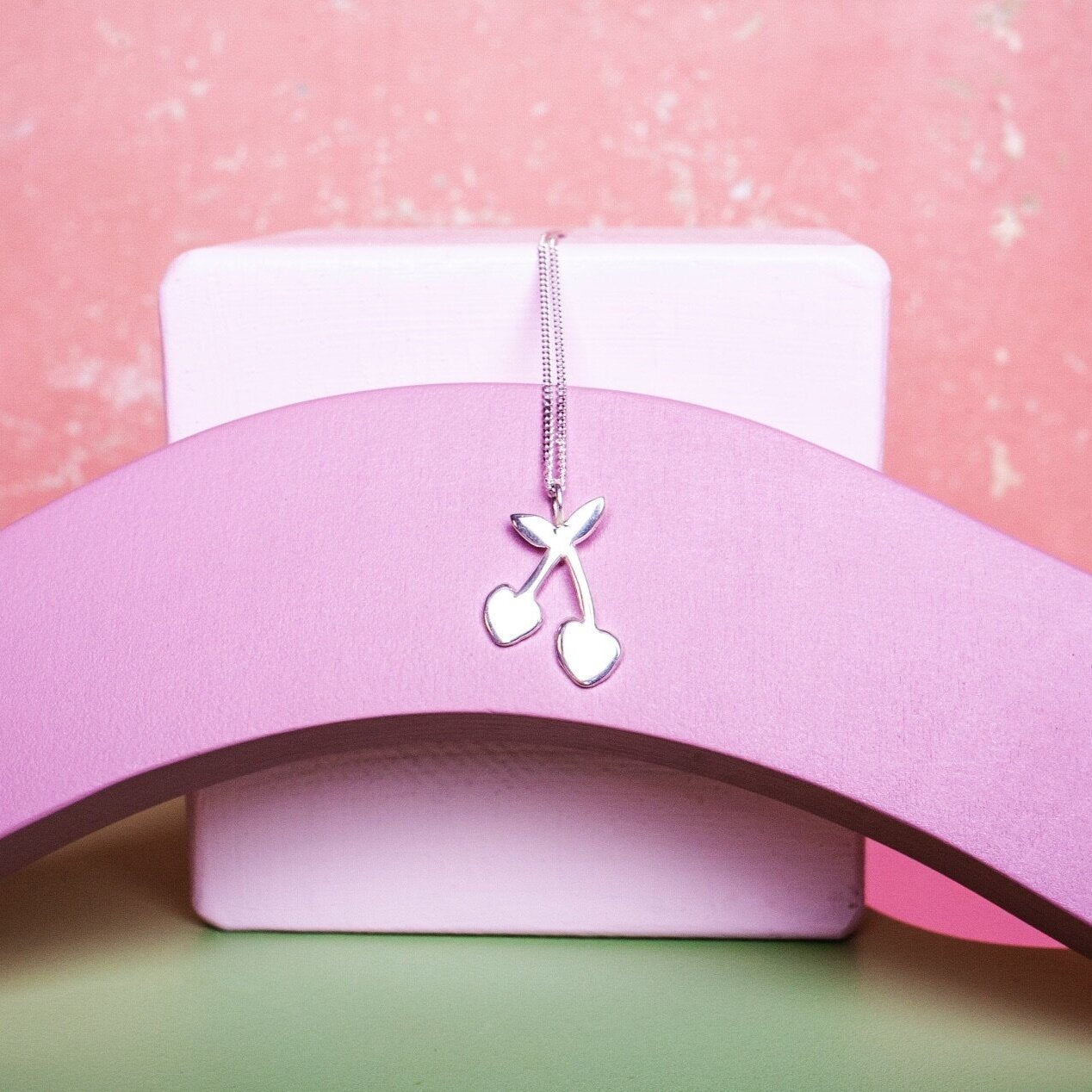 Close up of silver pendant necklace with a cherry shaped charm