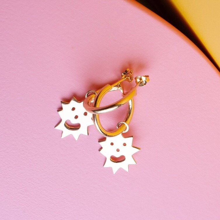 Close up of small hoop earrings with an irregular spikey shaped charm with a smiling face on