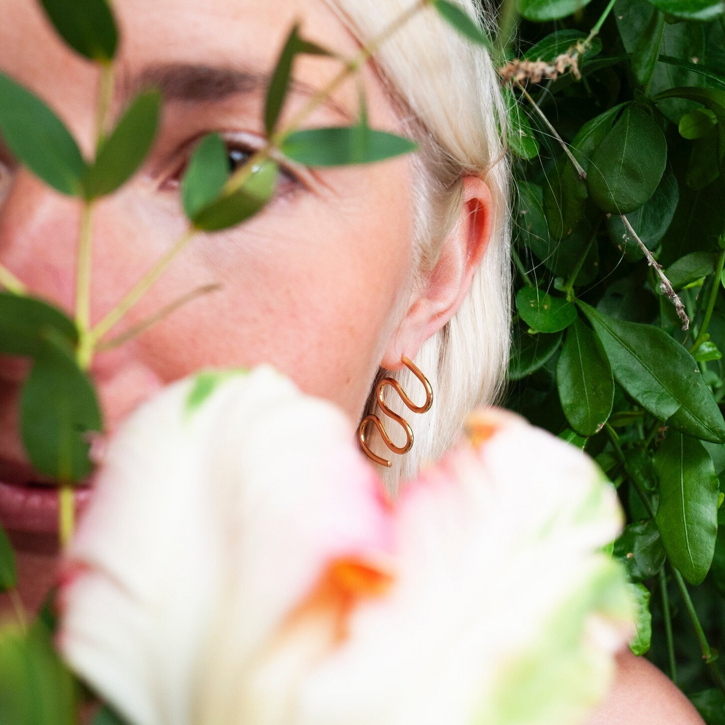 Woman wearing gold earring in the shape of a squiggle.
