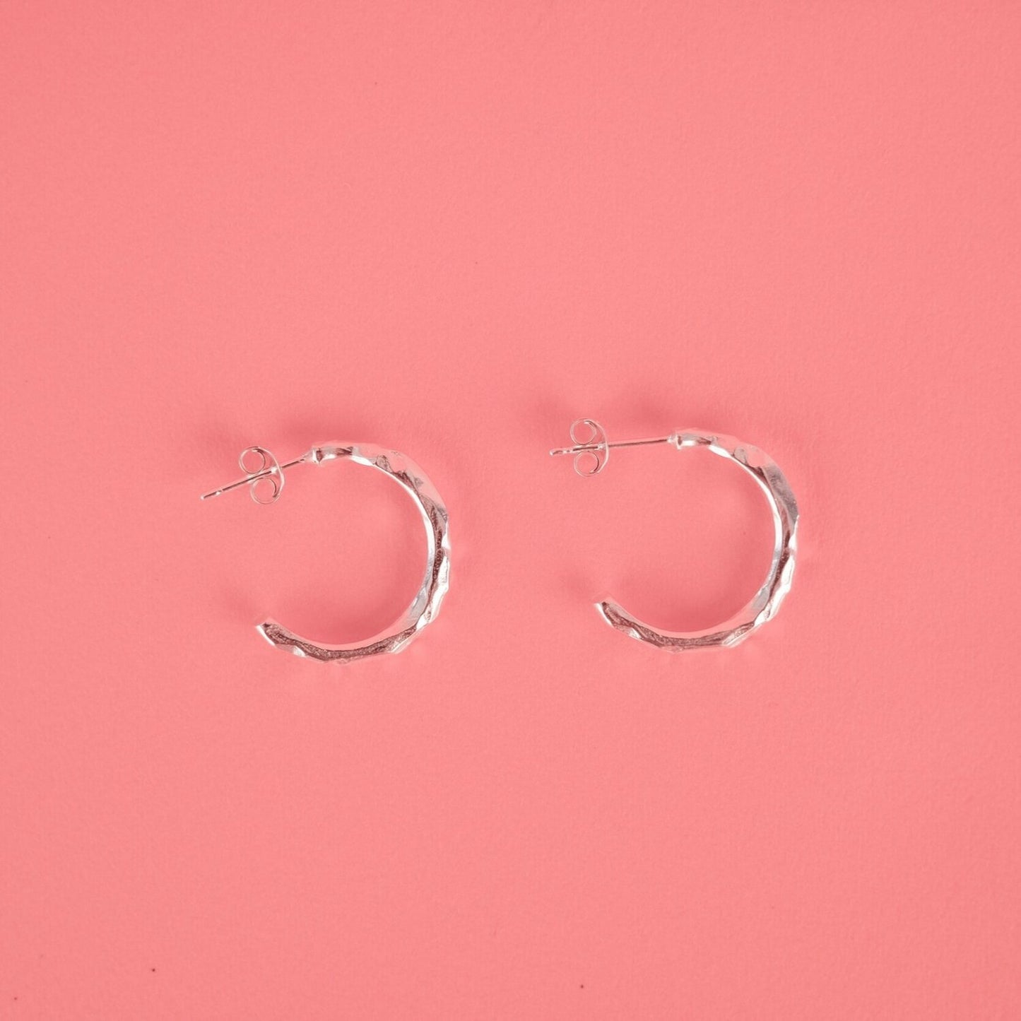Close up of small silver hoop earrings with a textured surface