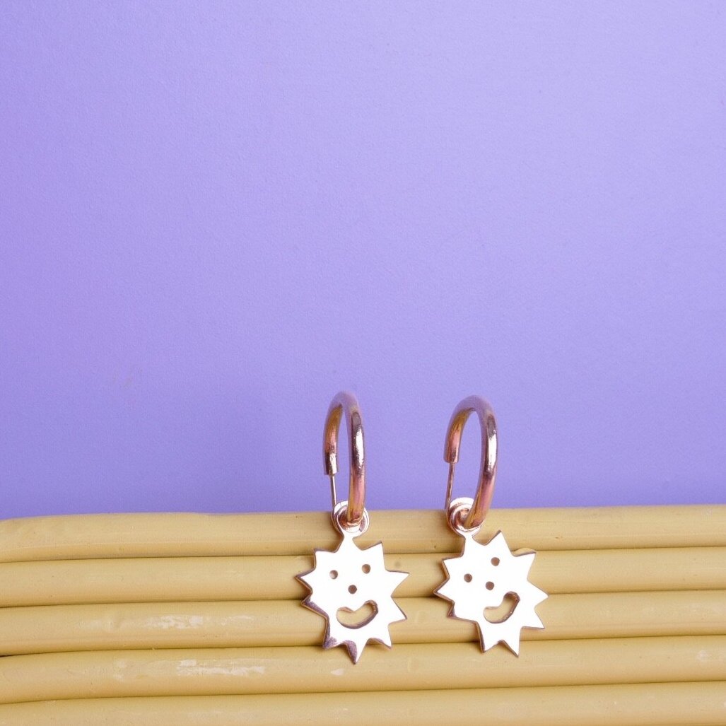 Close up of small hoop earrings with an irregular spikey shaped charm with a smiling face on