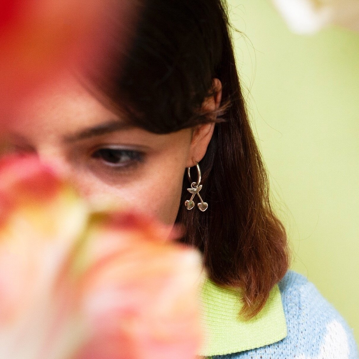 Woman wearing small hoop earring with a cherry charm hanging from it