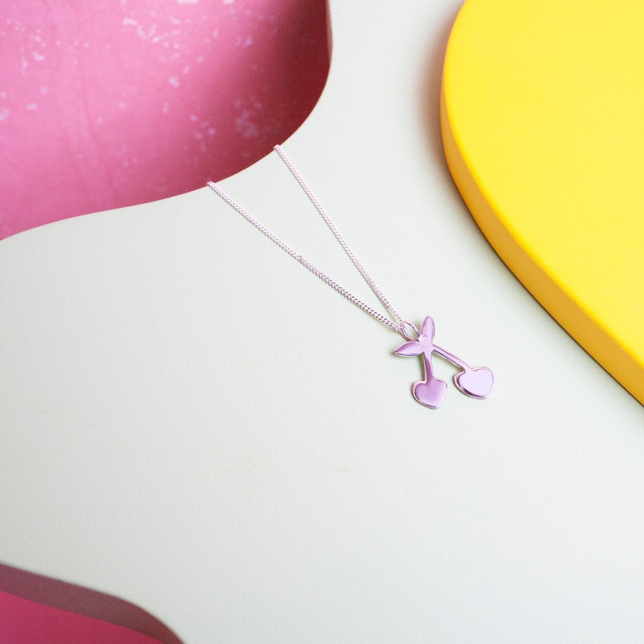 Close up of silver pendant necklace with a cherry shaped charm