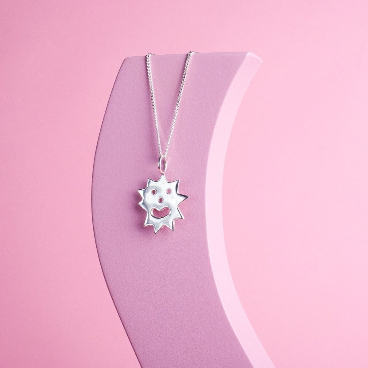 Close up of pendant necklace with a spikey irregular shaped charm with a smiley face on