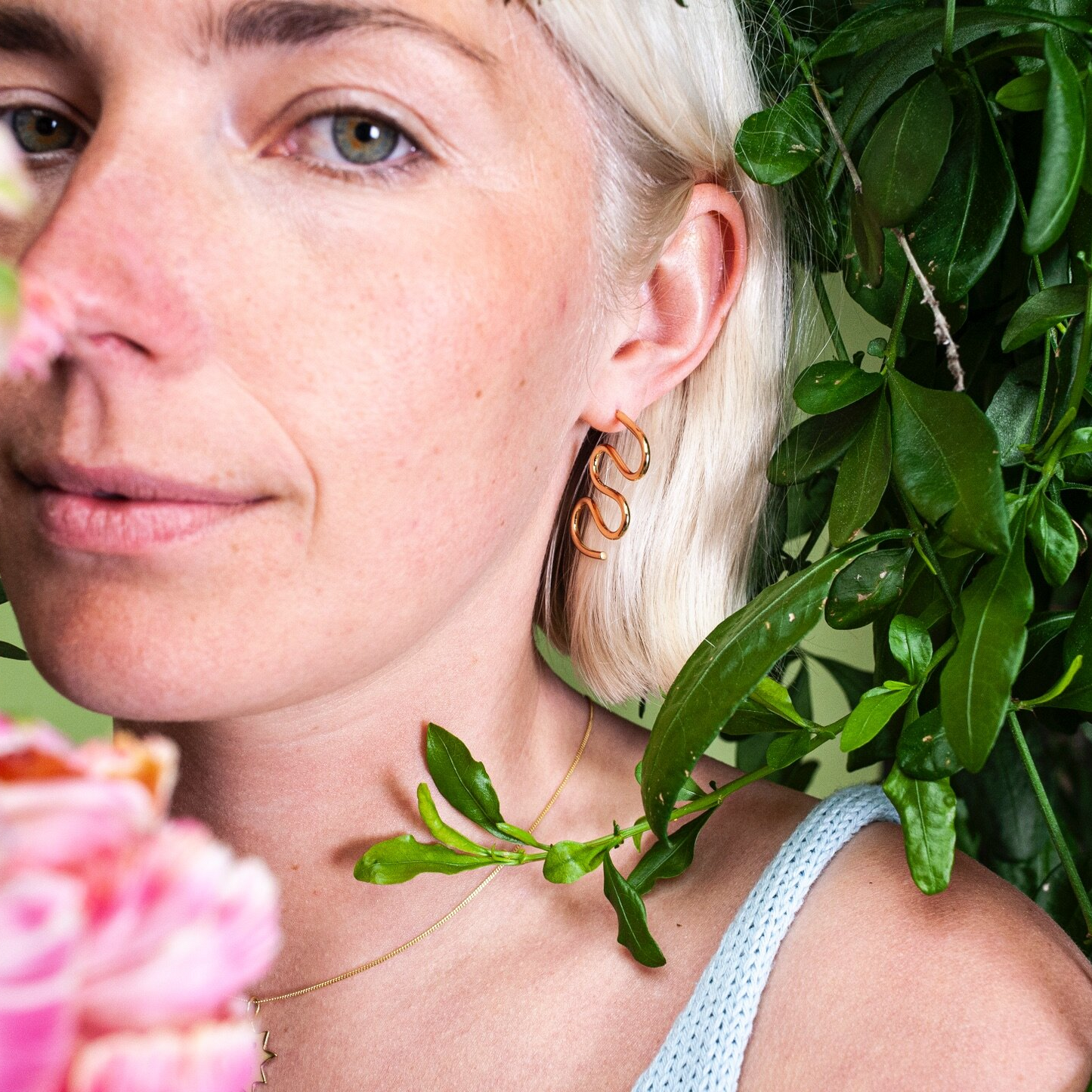 Close up of woman wearing gold earring in the shape of a squiggle