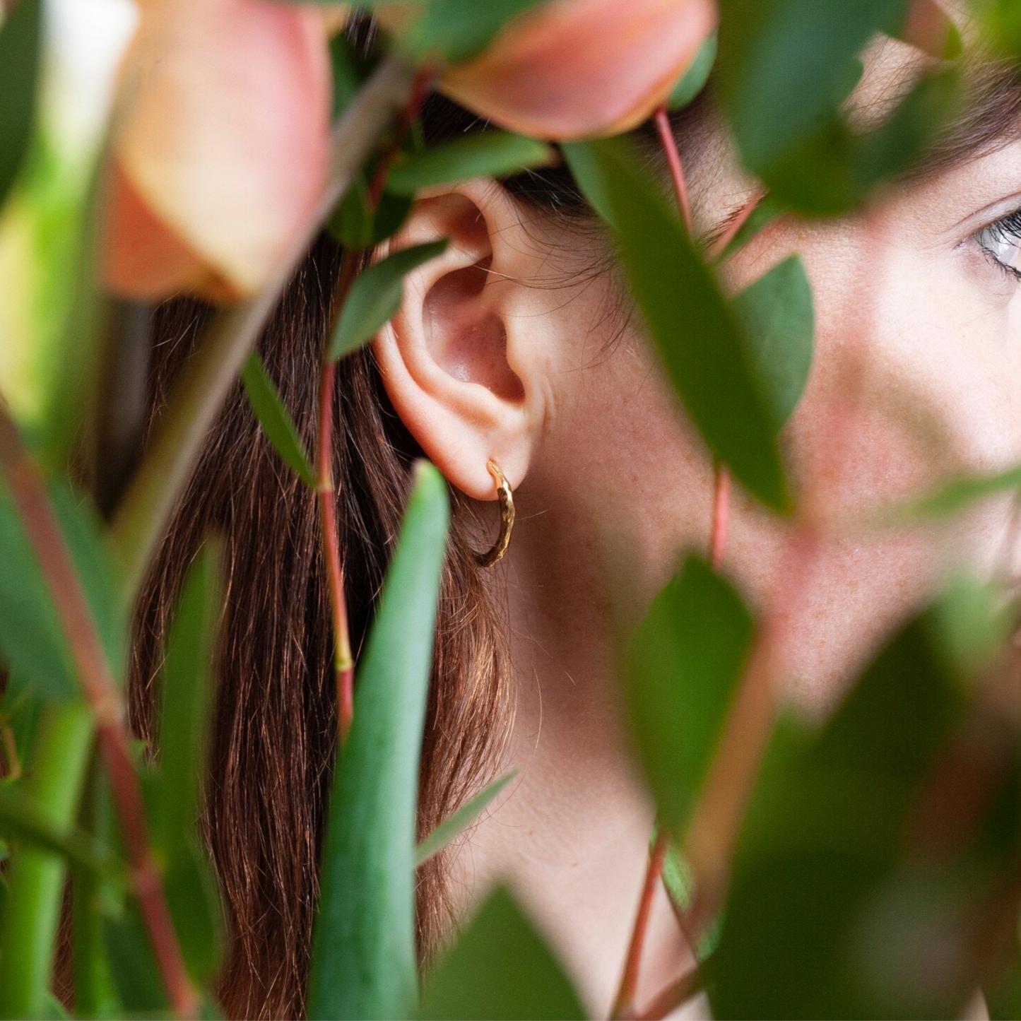 Close up of woman wearing small gold hoop earrings with a textured surface