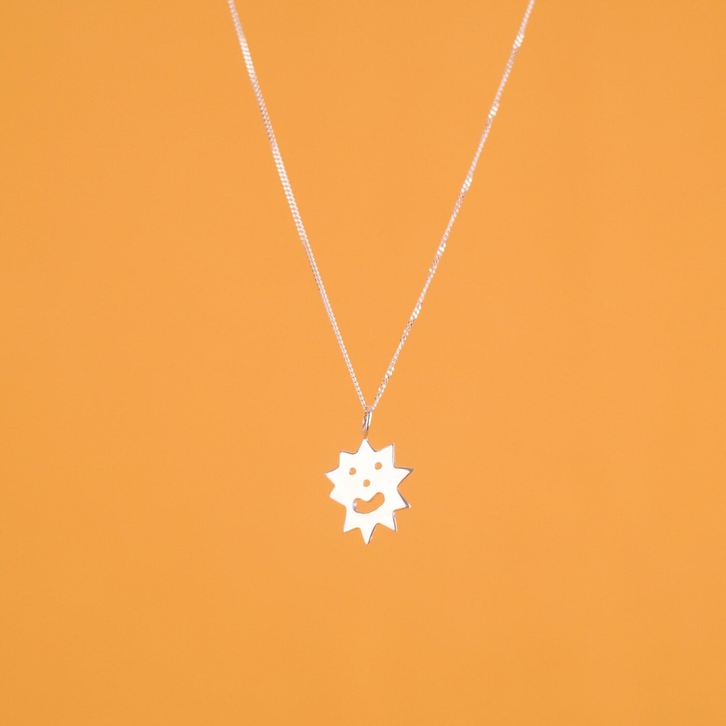 Close up of pendant necklace with a spiky irregular shaped charm with a smiley face on