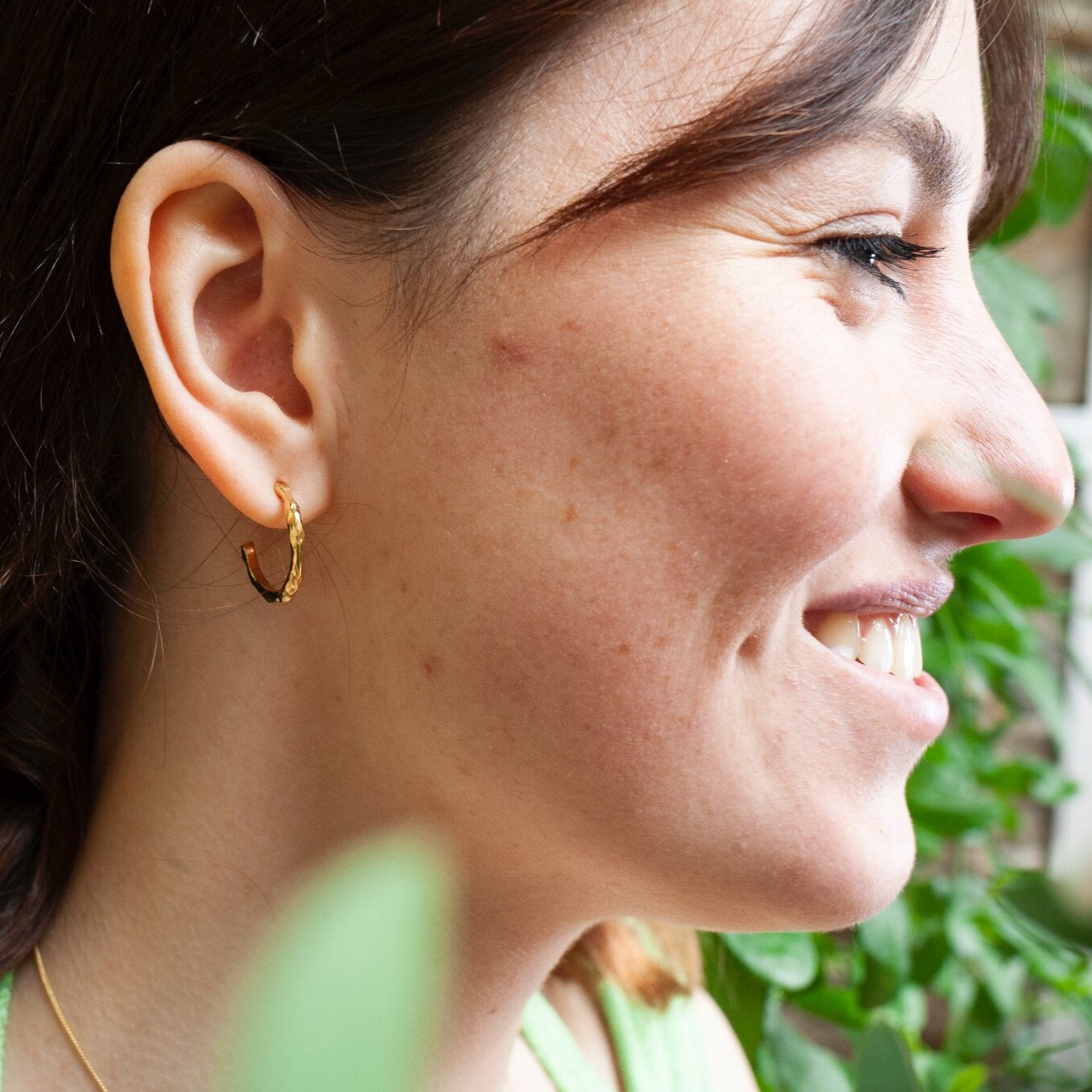 Close up of woman wearing small gold hoop earring with a textured surface